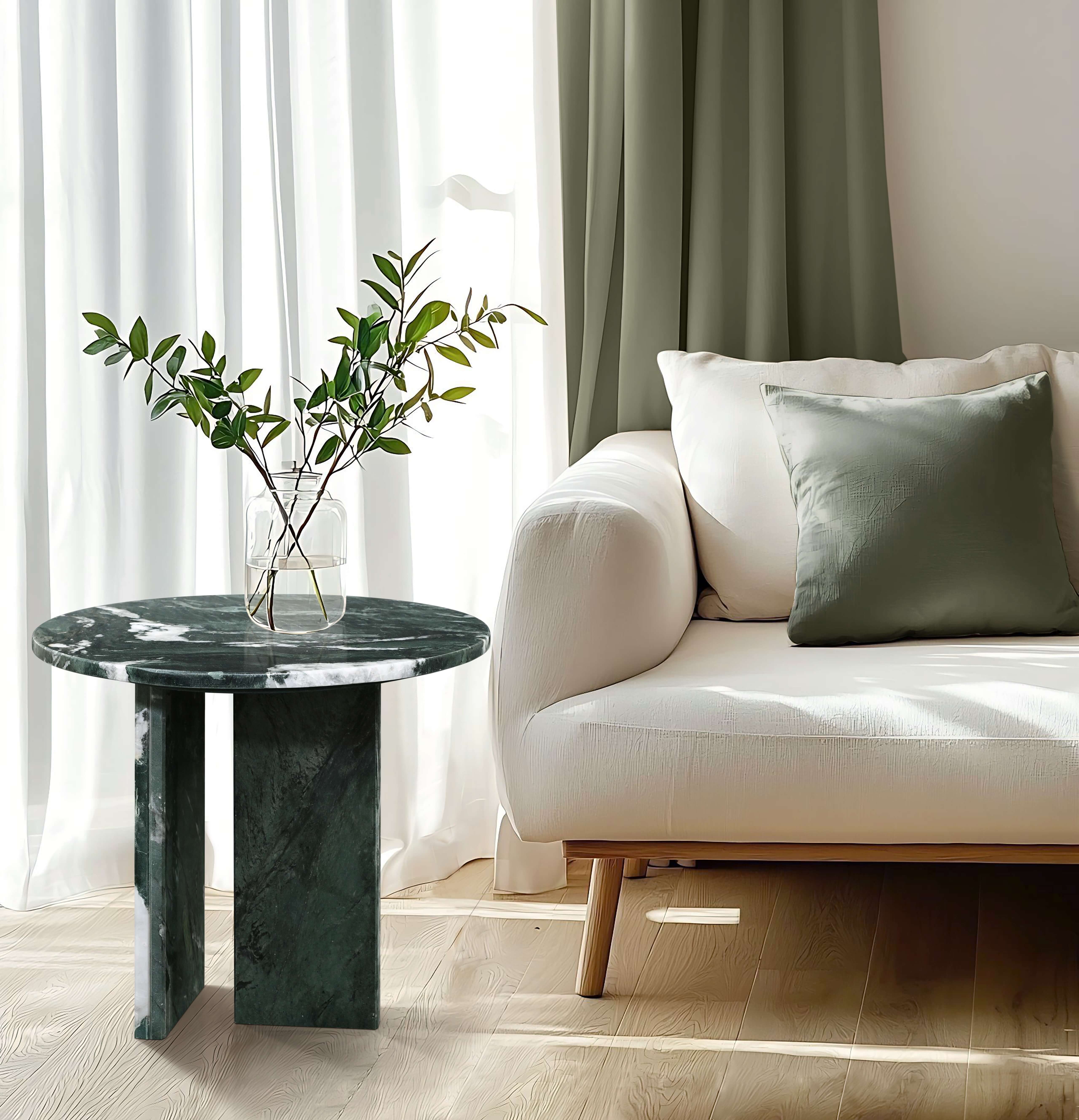 A modern green stone side table styled next to a beige sofa in a bright living room, holding a vase with greenery.