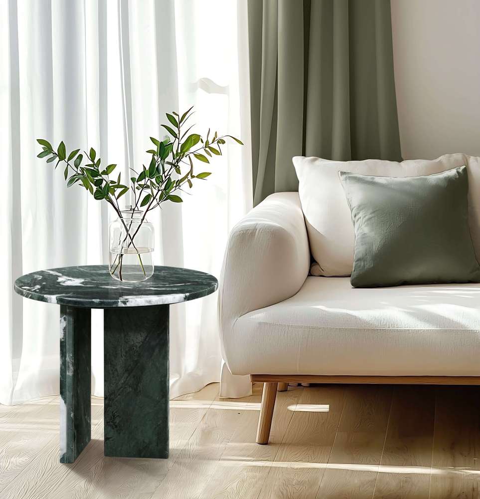 A modern green stone side table styled next to a beige sofa in a bright living room, holding a vase with greenery.