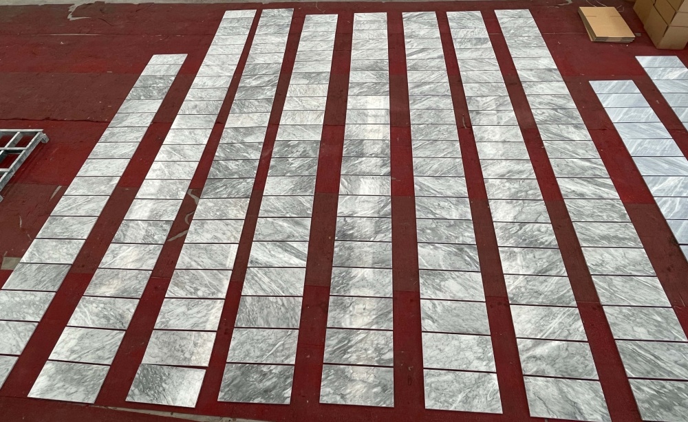 Factory production layout of 12x24 Carrara Gray polished marble tiles, showcasing the 100% natural and unique veins of each piece during quality inspection.