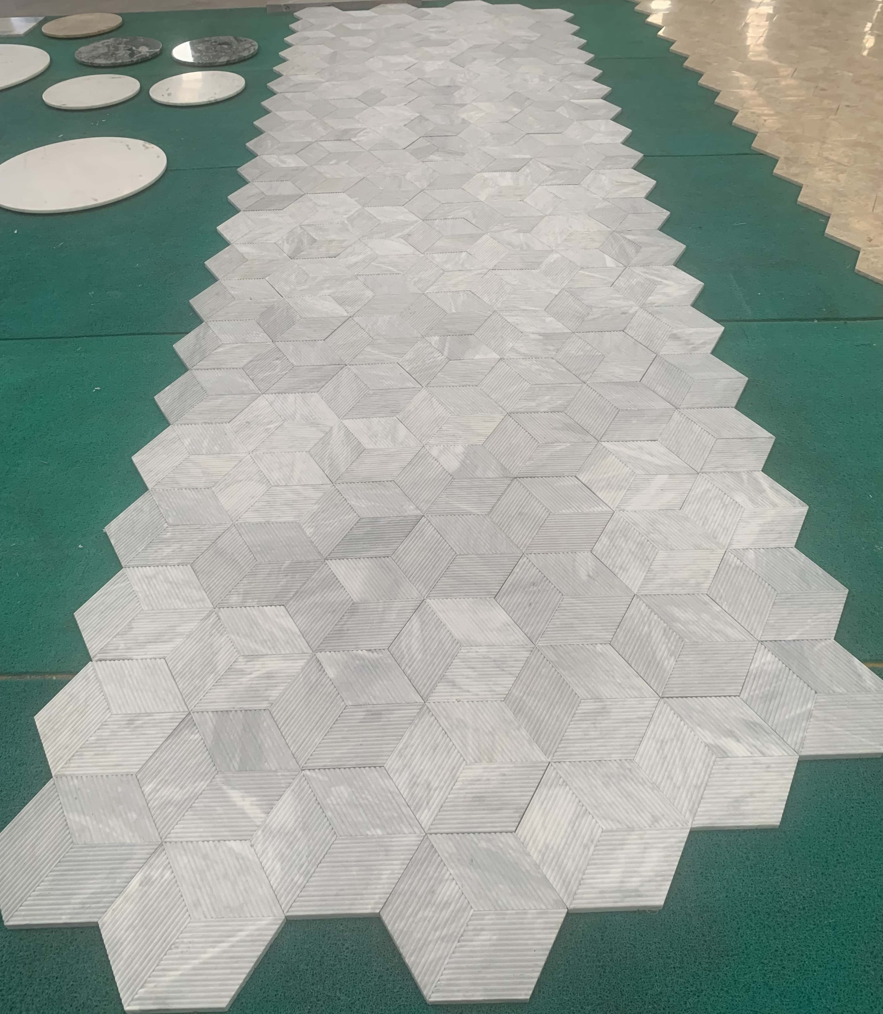 Real-world large-scale layout of 100% natural Carrara Gray fluted marble tiles, displaying unique natural stone variations.