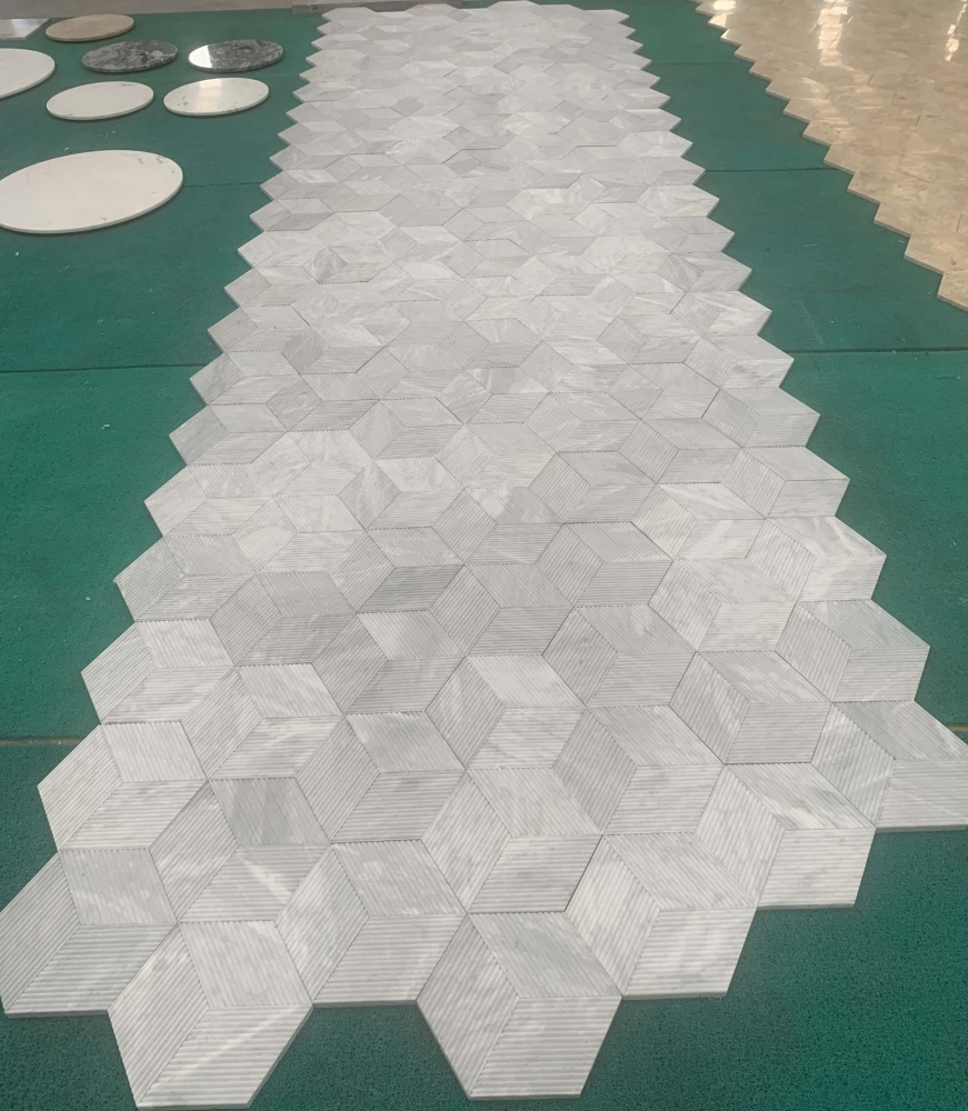 Real-world large-scale layout of 100% natural Carrara Gray fluted marble tiles, displaying unique natural stone variations.