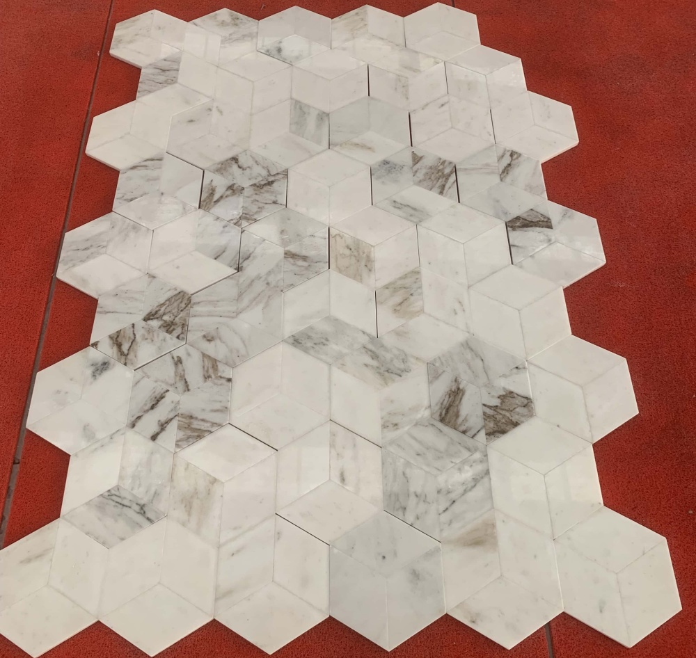 Real-world factory display of genuine Snow Mountain White hexagon marble tiles, showcasing the 100% unique natural stone veining and striking 3D visual effect.
