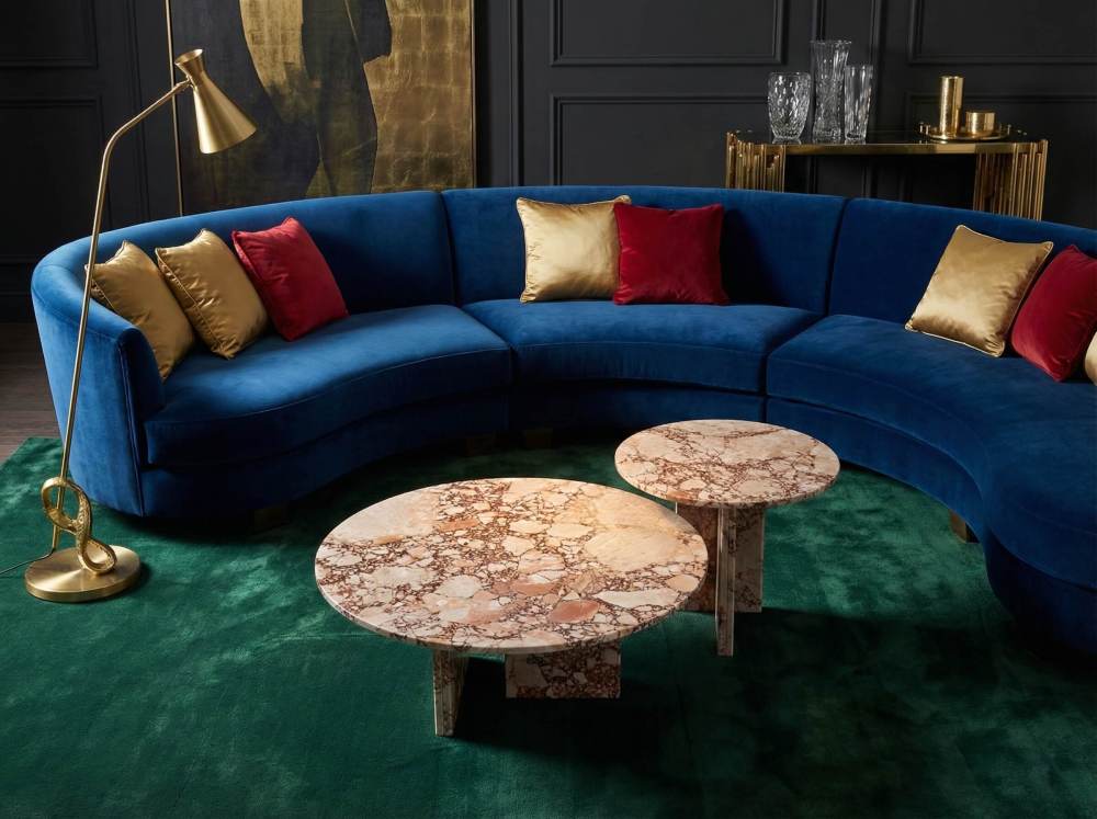 Luxury living room featuring a curved blue velvet sofa and our 2-piece diamond pink real marble cocktail table set. The natural stone's unique veins stand out beautifully against jewel-toned interior design.