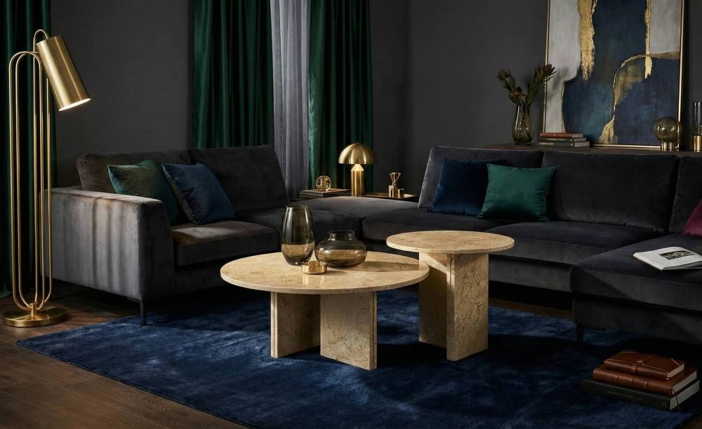 The premium beige marble coffee table set stands out in a moody living room setting with dark grey seating and emerald green accents. Shipped securely with custom damage-proof packaging.