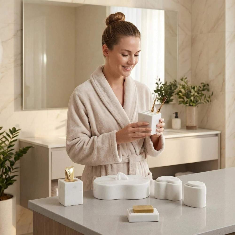 A smiling woman in a bathrobe holding the unique natural marble toothbrush holder from the Snow Mountain White bathroom accessories set in a bright, contemporary bathroom.