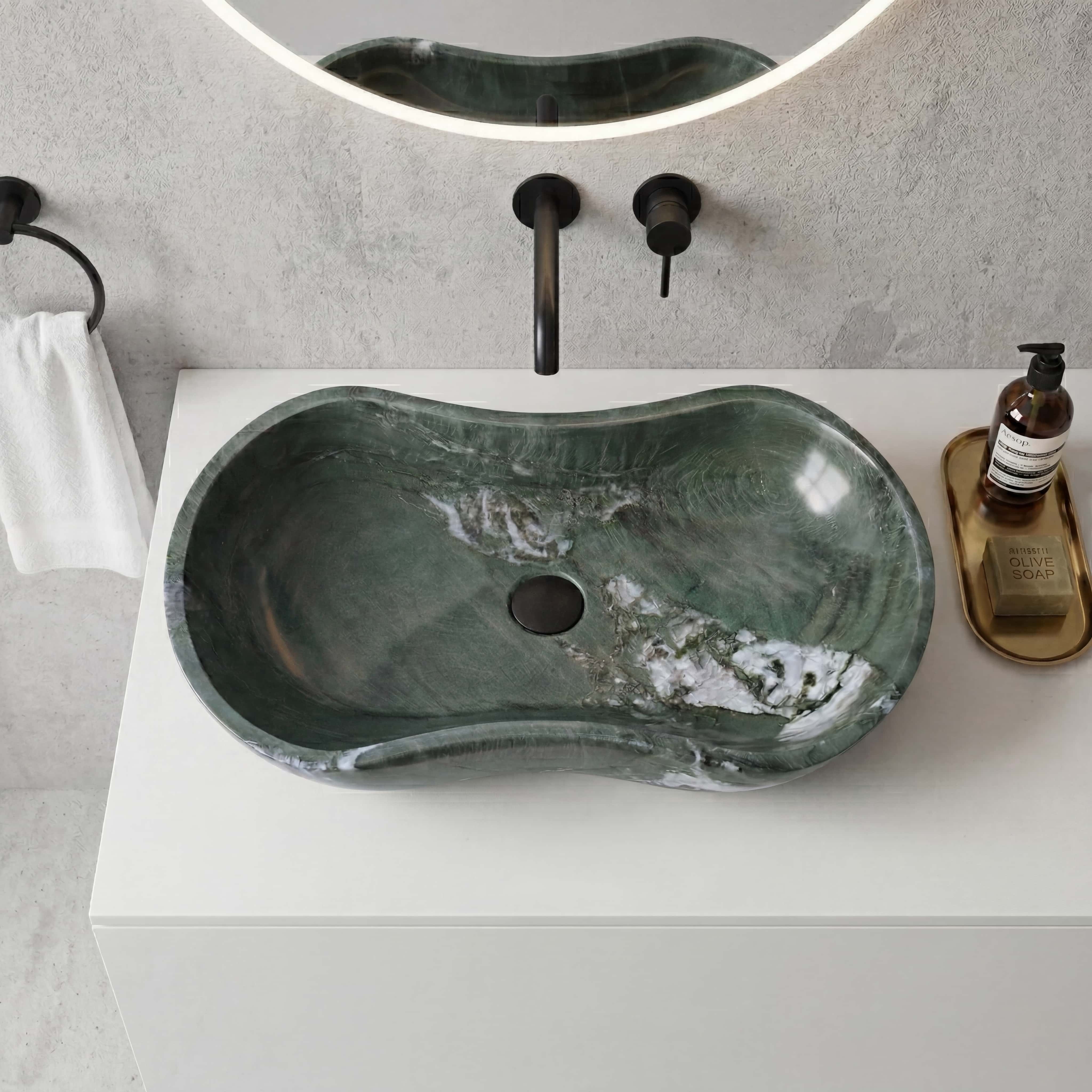 Top view of wavy Diamond Green natural marble vessel sink featuring organic curves and white veining, paired with matte black wall-mounted faucet on white quartz countertop and grey textured wall.