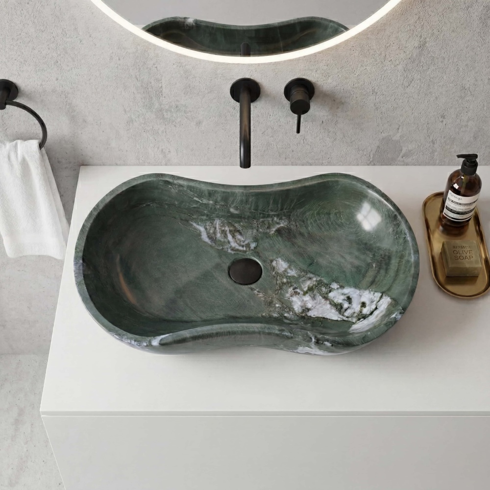Top view of wavy Diamond Green natural marble vessel sink featuring organic curves and white veining, paired with matte black wall-mounted faucet on white quartz countertop and grey textured wall.
