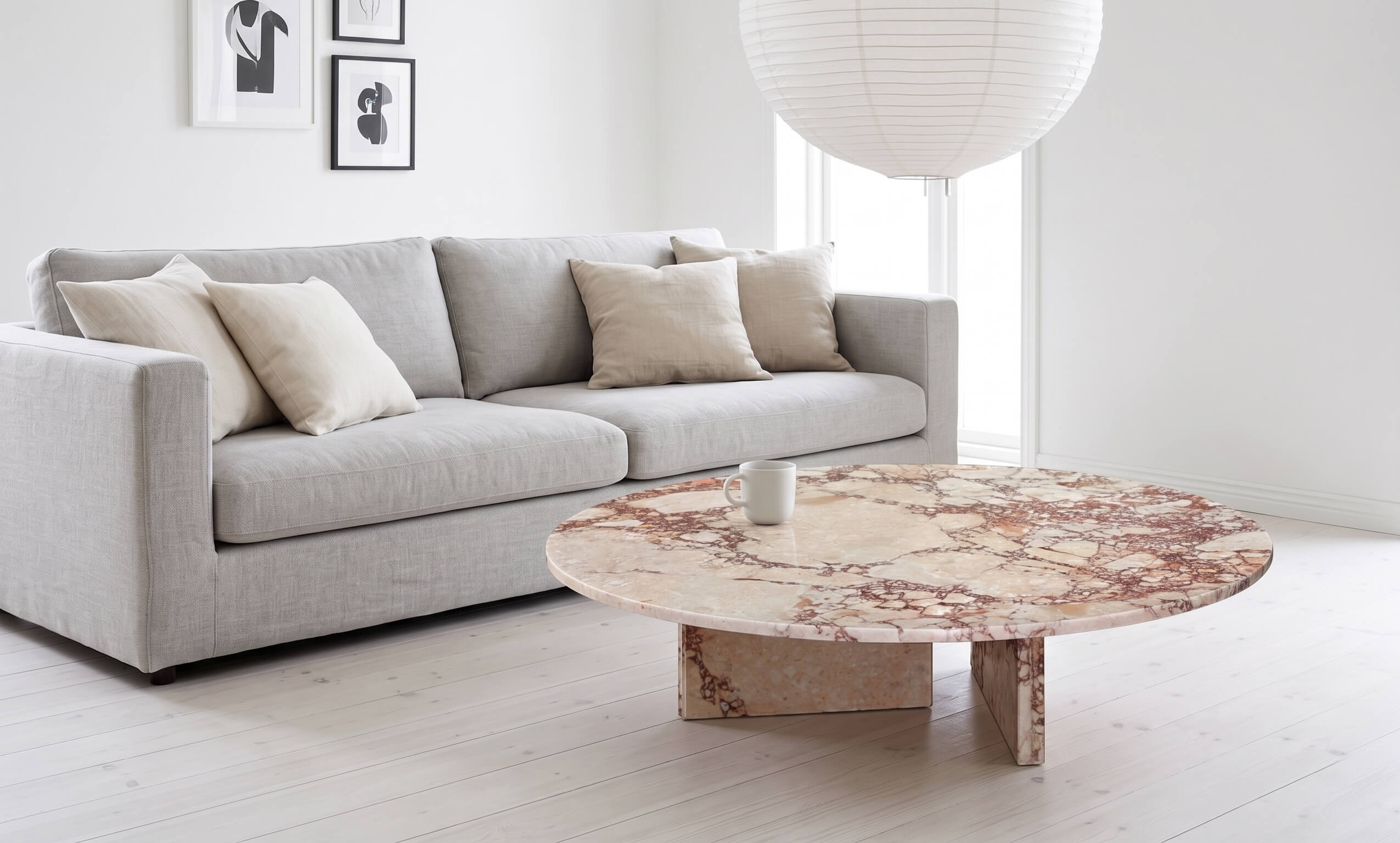 Minimalist living room setting featuring a round Diamond Pink marble table with a polished surface against white walls and light oak flooring.