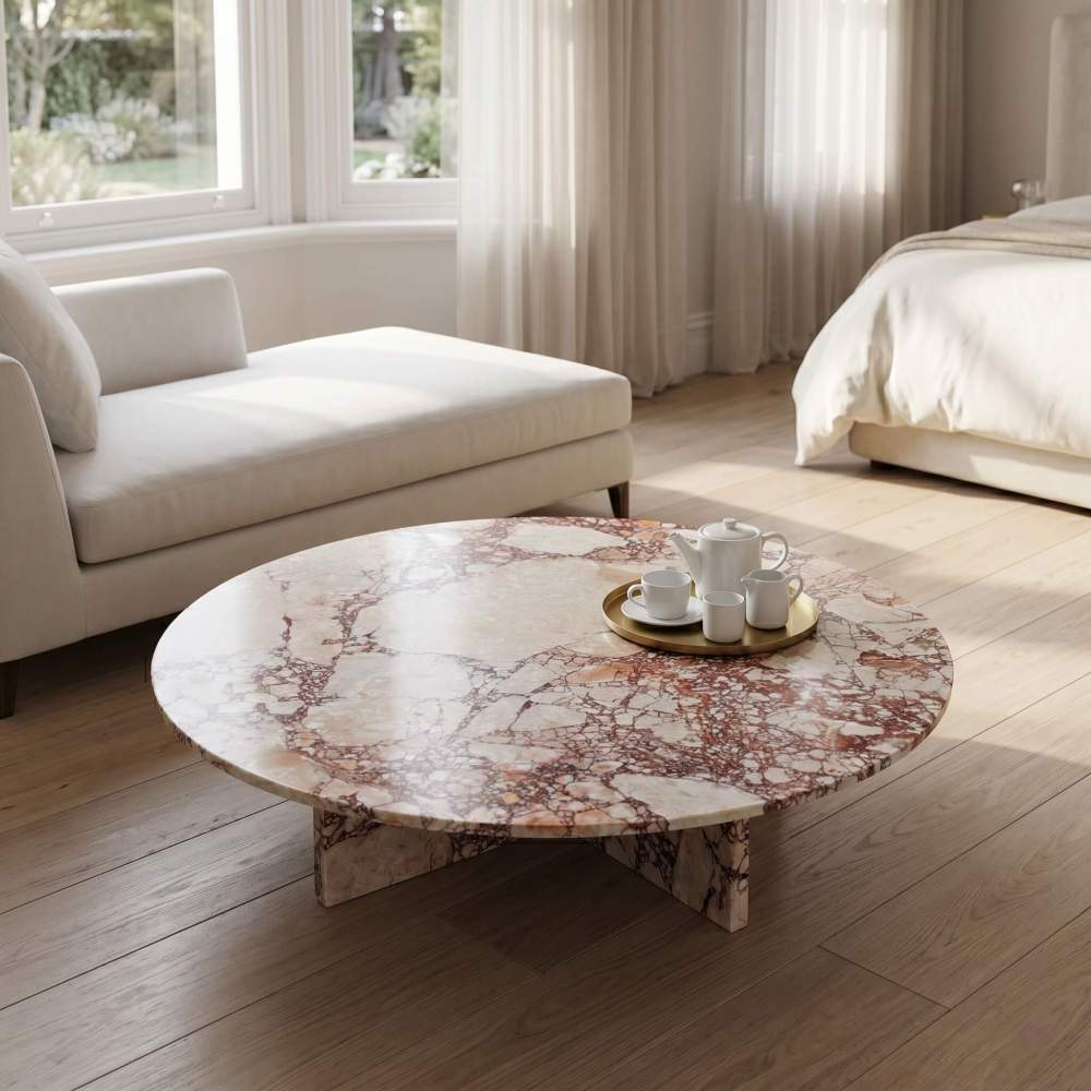 Diamond Pink natural marble coffee table used as a luxury bedside surface in a minimalist bedroom with floor-to-ceiling windows and light oak flooring.