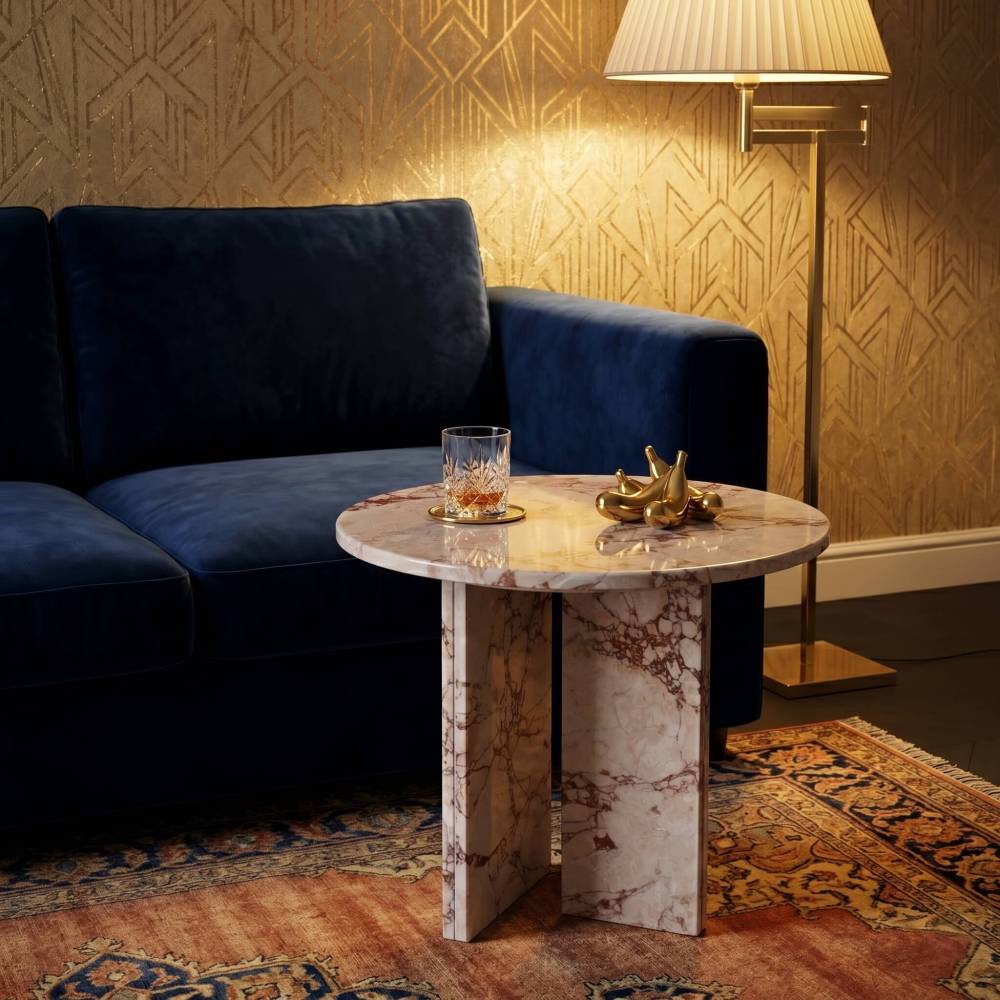 Diamond Pink marble side table in an Art Deco glam living room — navy blue velvet sofa, gold geometric patterned wallpaper, crystal whiskey glass and gold decorative objects on polished marble tabletop, warm directional lamp illuminating natural stone veining.