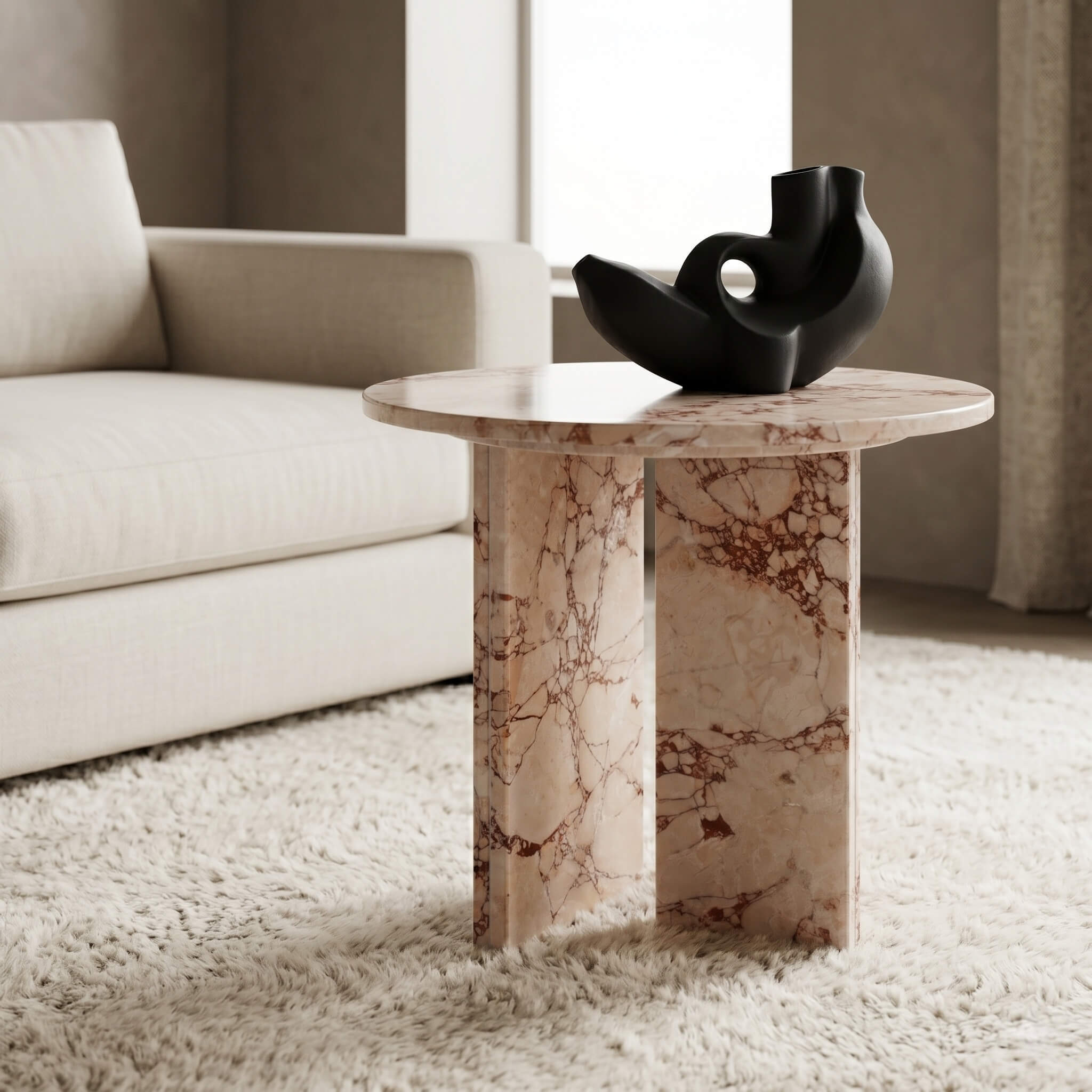 Diamond Pink natural marble round side table close-up — matte black abstract ceramic sculpture on polished stone surface, dual-panel base with natural burgundy veining visible on shaggy white rug, beside cream linen sofa.