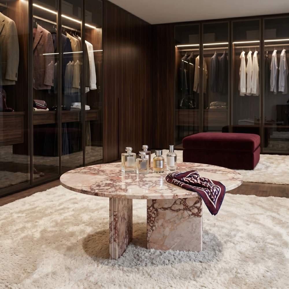 Diamond Pink marble round coffee table in a luxury walk-in closet — dark walnut cabinetry with LED strip lighting, cream shaggy rug, perfume bottles and silk scarf displayed on polished marble tabletop.