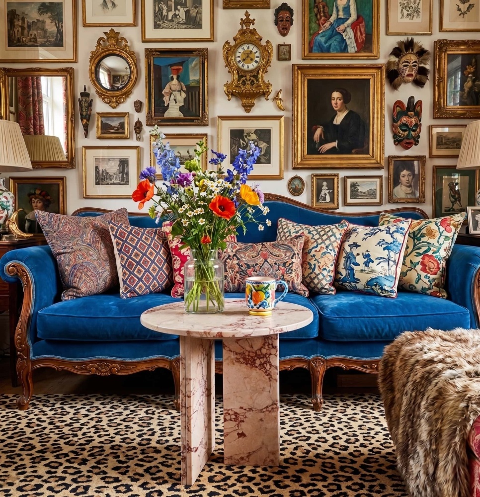 Diamond Pink natural marble side table centered before a blue velvet French Louis XV sofa in a maximalist gallery wall living room — leopard print rug, gilded frames, and fresh floral arrangement.