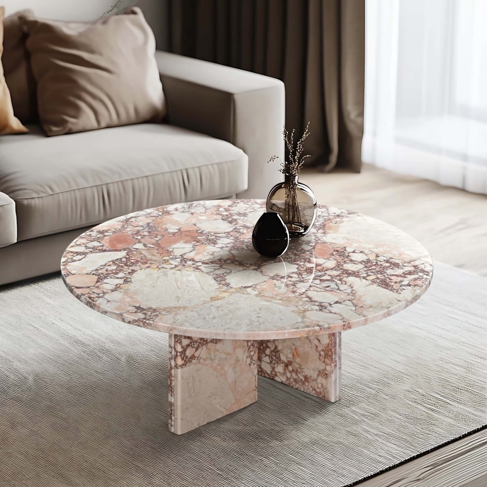 Overhead angle view of Diamond Pink marble coffee table in a modern minimalist living room — light gray ribbed-texture area rug, beige modular sofa, matte black ceramic sculpture and globe-form glass vase with dried botanicals on full-view polished marble tabletop.