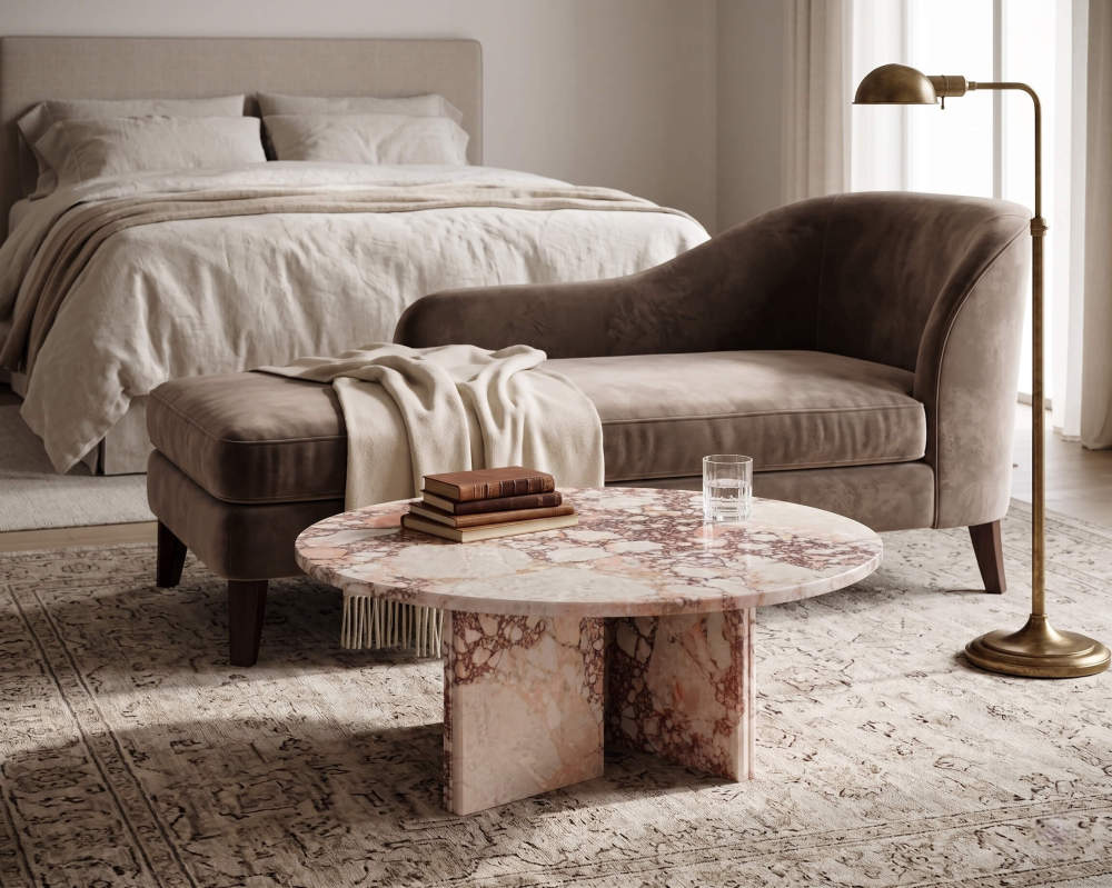 Diamond Pink marble coffee table beside a velvet chaise longue in a neoclassical bedroom — warm brass floor lamp, Persian-style area rug, linen bedding, stacked leather-bound books on marble surface, raking natural light from side window.
