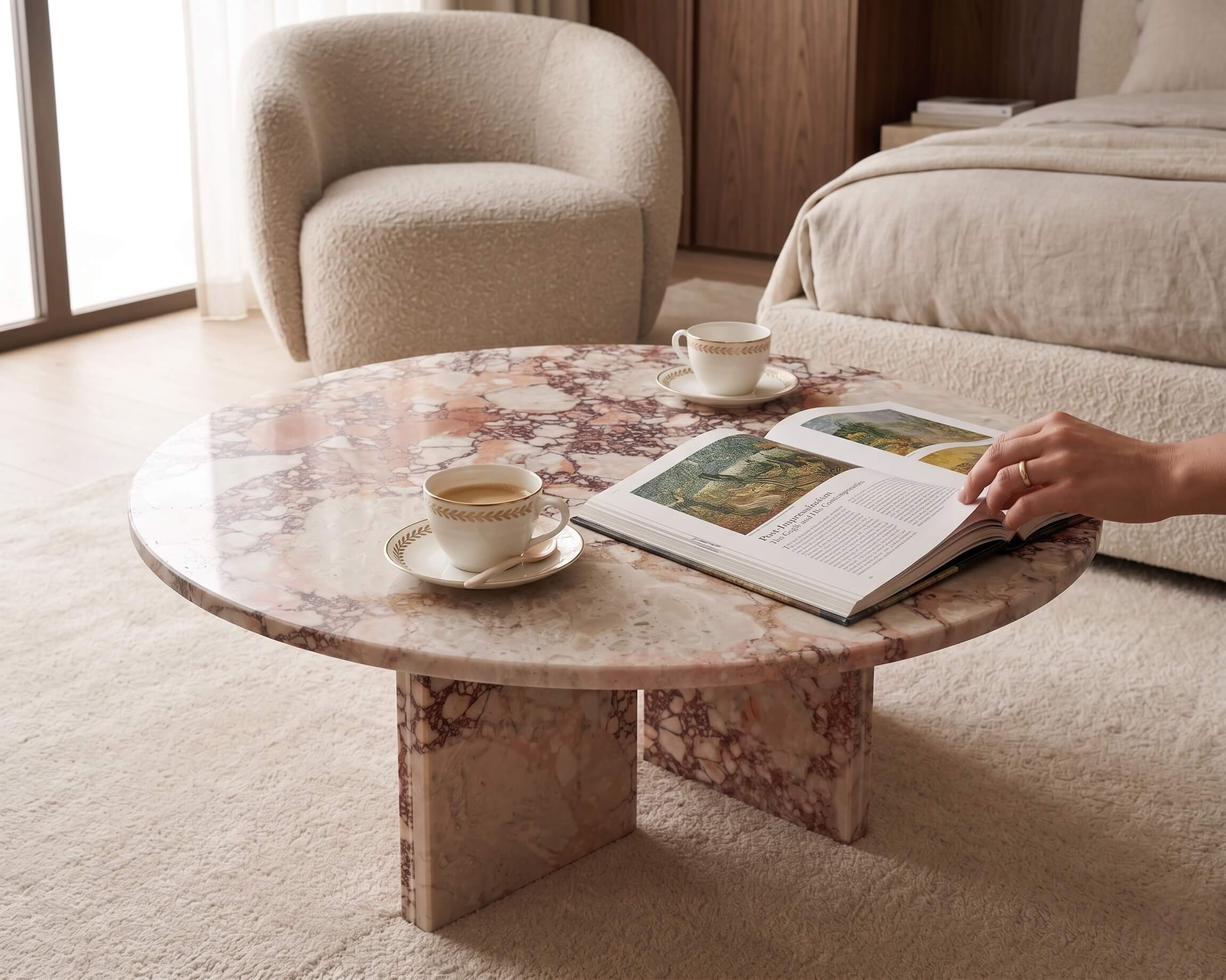 A round pink marble accent table paired with a white bouclé armchair in a sun-drenched Japandi bedroom, highlighting its organic texture.