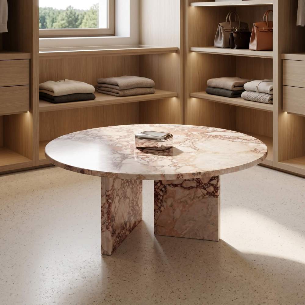 A polished pink marble center table acting as a sophisticated centerpiece in a high-end walk-in closet featuring designer accessory displays.
