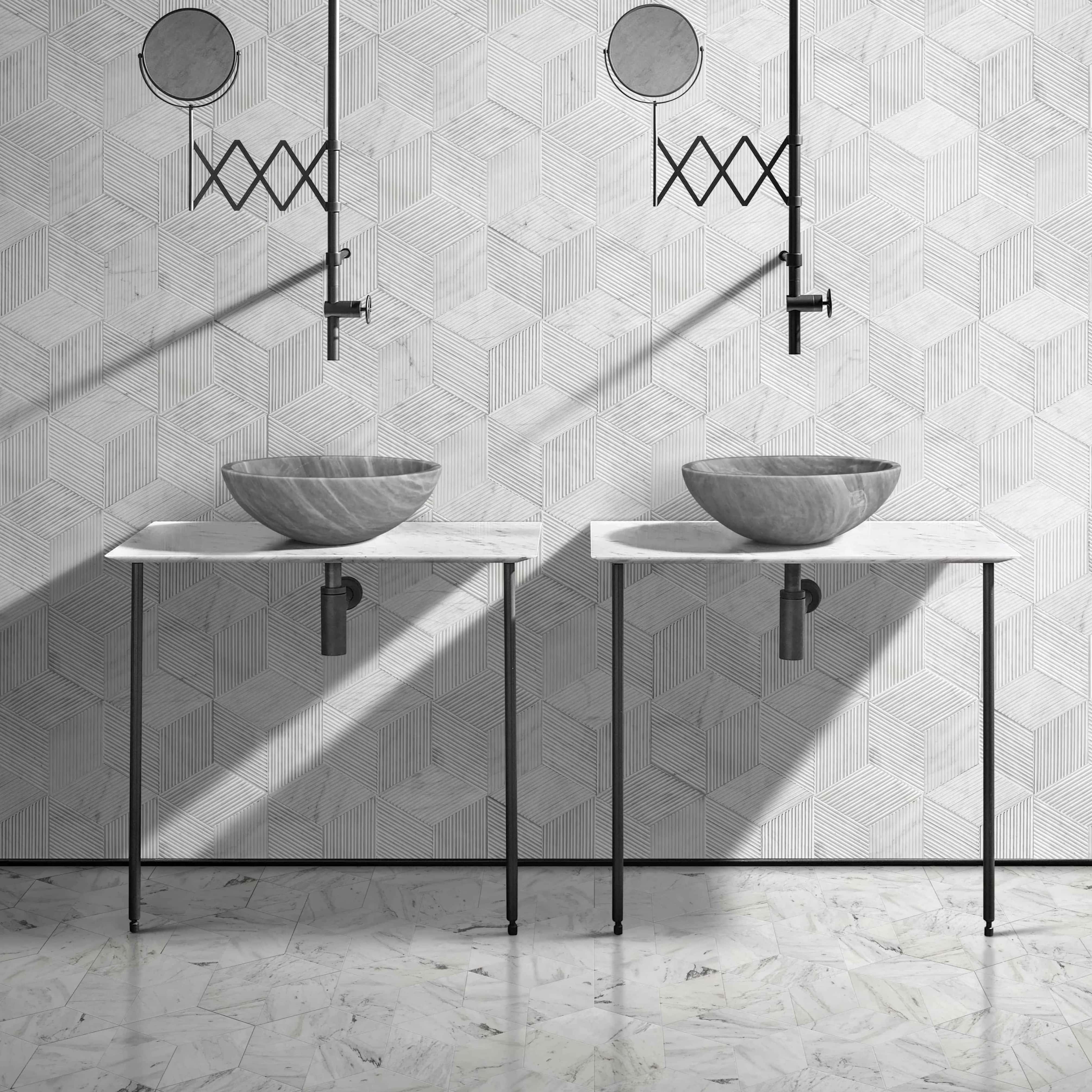 Two Carrara gray marble round vessel sinks on white marble console tables with black metal legs in an editorial minimalist bathroom, set against Snow Mountain White hexagon OL-textured finished marble wall tiles forming a 3D cube optical pattern, Snow Mountain White hexagon polished marble floor tiles with Carrara-like veining, exposed black metal P-traps and adjustable round shaving mirrors, directional natural light casting architectural shadows.
