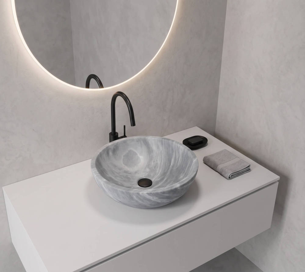 Single Carrara gray marble round vessel sink as sculptural focal point on a pure white handle-less floating vanity, matte black gooseneck faucet, halo-lit round mirror with backlit LED ring, textured white plaster wall, minimal styling with single black marble soap dish, gallery-aesthetic bathroom.