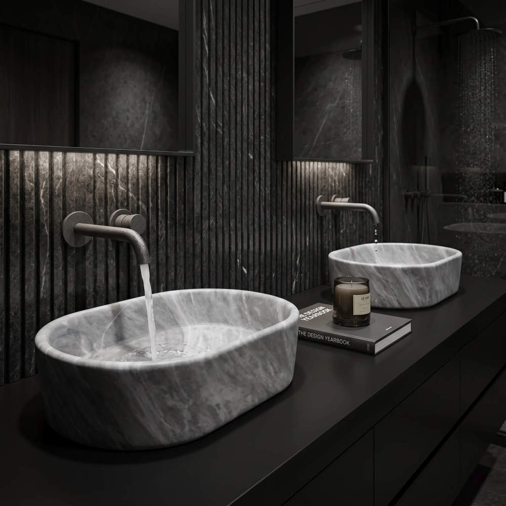 Two oval Carrara gray marble vessel sinks on matte black counter against fluted dark marble walls with gunmetal wall faucets.