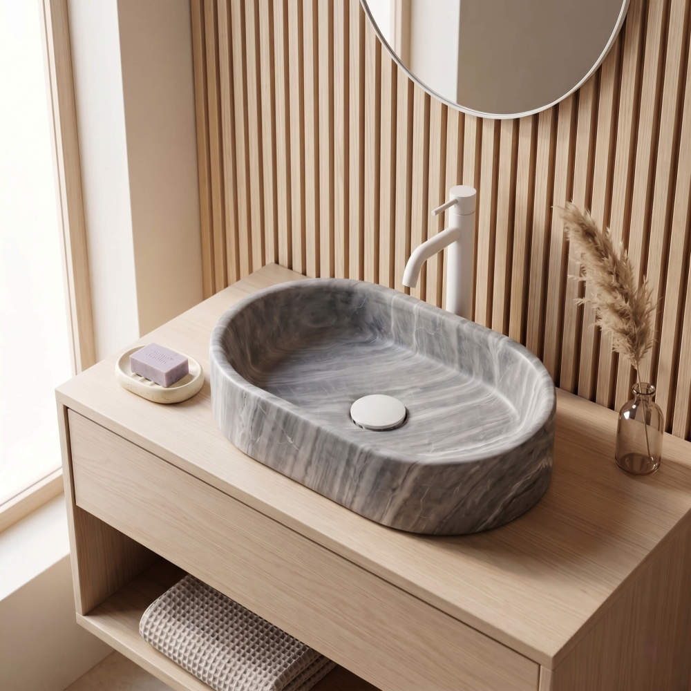 Oval Carrara gray marble vessel sink on oak vanity against vertical wood slat wall with matte white faucet and pampas styling.