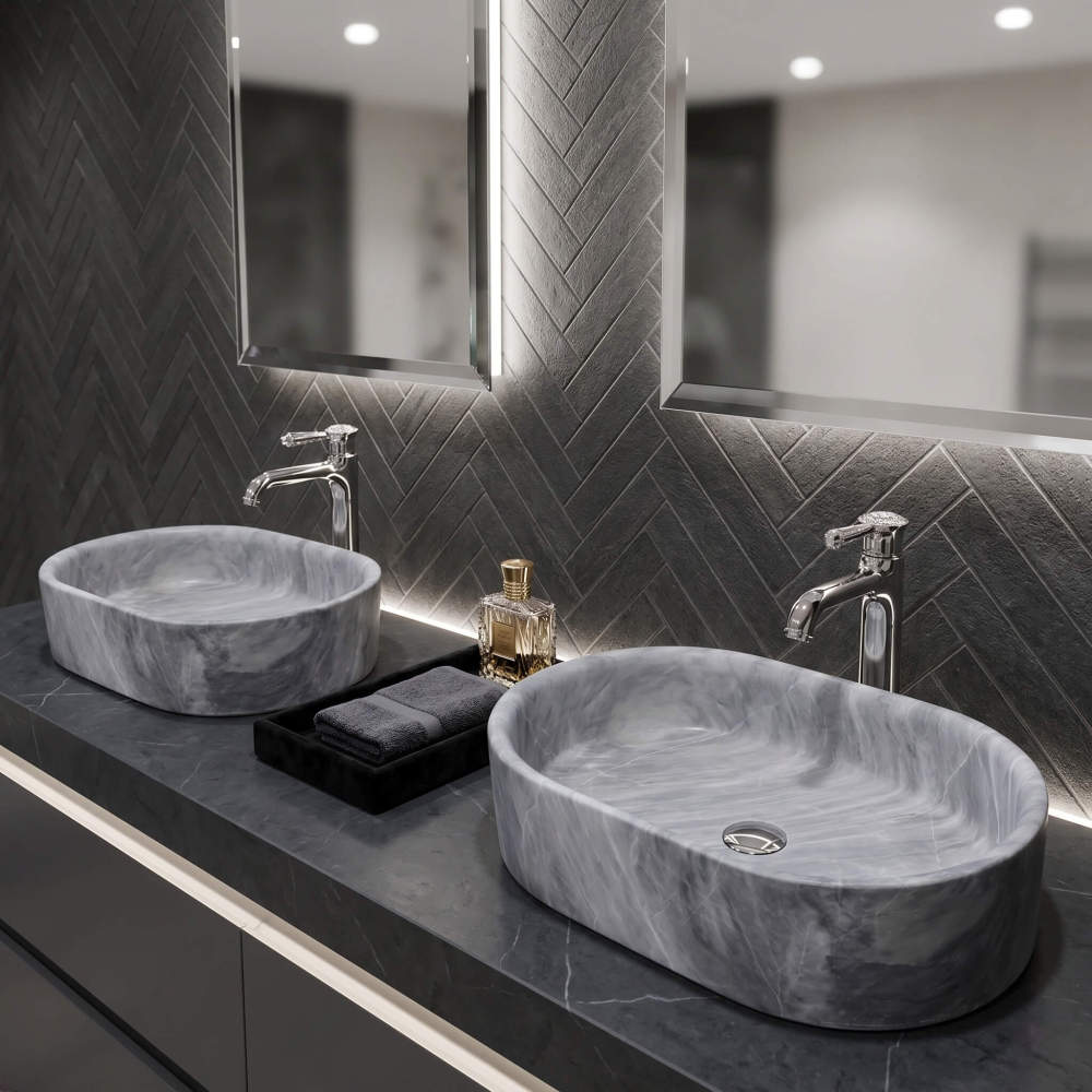 Pair of oval Carrara gray marble vessel sinks on dark marble counter with herringbone backsplash and polished chrome faucets.
