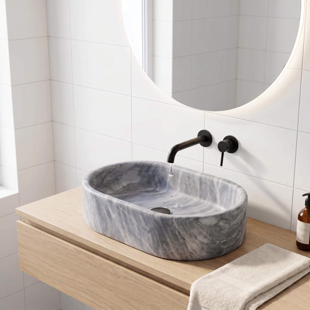 Oval Carrara gray marble vessel sink on oak floating vanity with matte black wall faucet and round LED mirror.