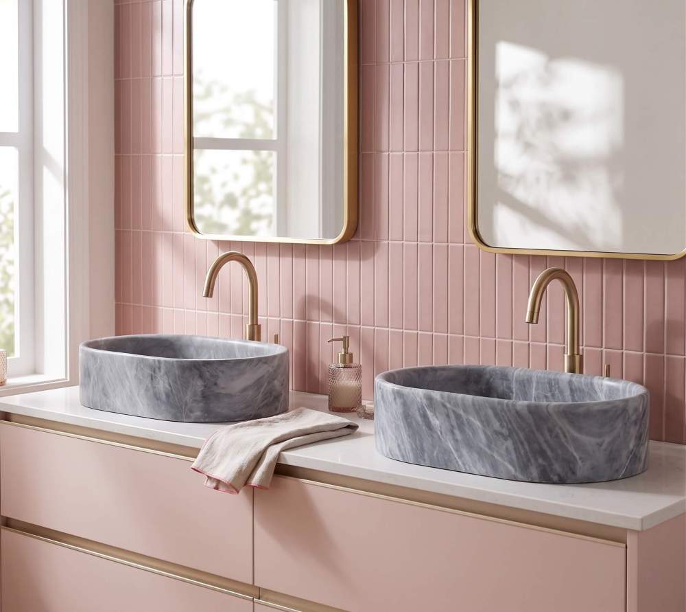 Oval Carrara gray marble vessel sinks on white quartz over a pink vanity with kit-kat tile and brass gooseneck faucets.