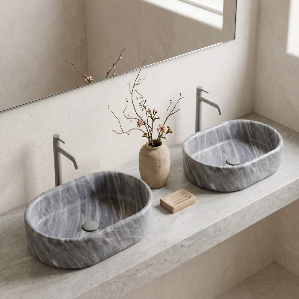 Oval Carrara gray marble vessel sinks on travertine counter in a wabi-sabi bath with microcement walls and matte beige faucets.
