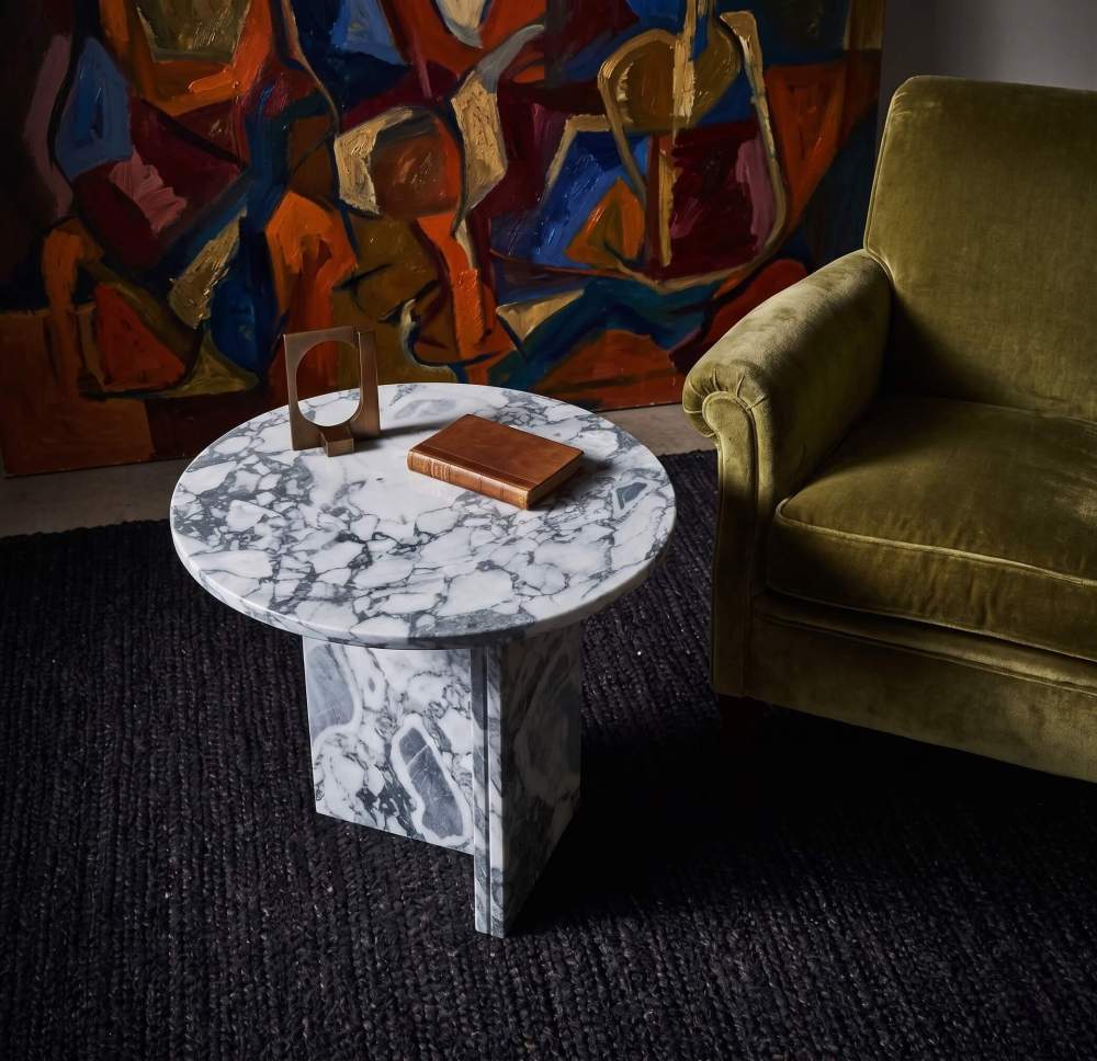 Cloudy blue marble side table in curated art lounge with olive velvet armchair, abstract oil painting backdrop, leather-bound book, and brass sculpture.