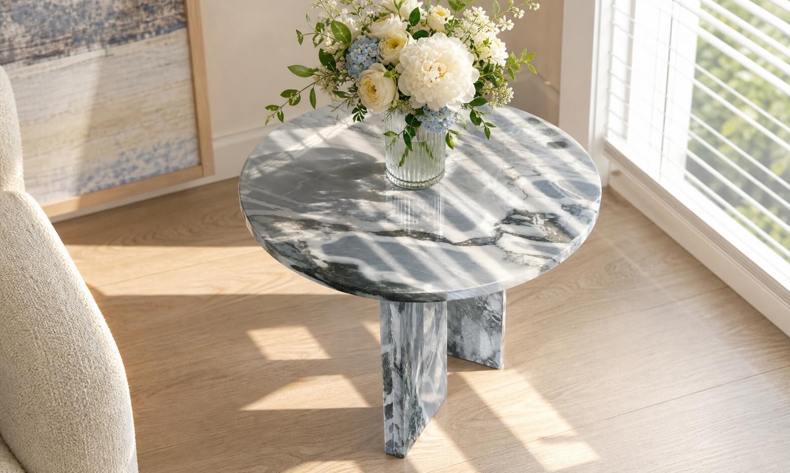 Cloudy blue marble side table topped with white peony, blue hydrangea, and rose bouquet in ribbed glass vase by sunlit window.