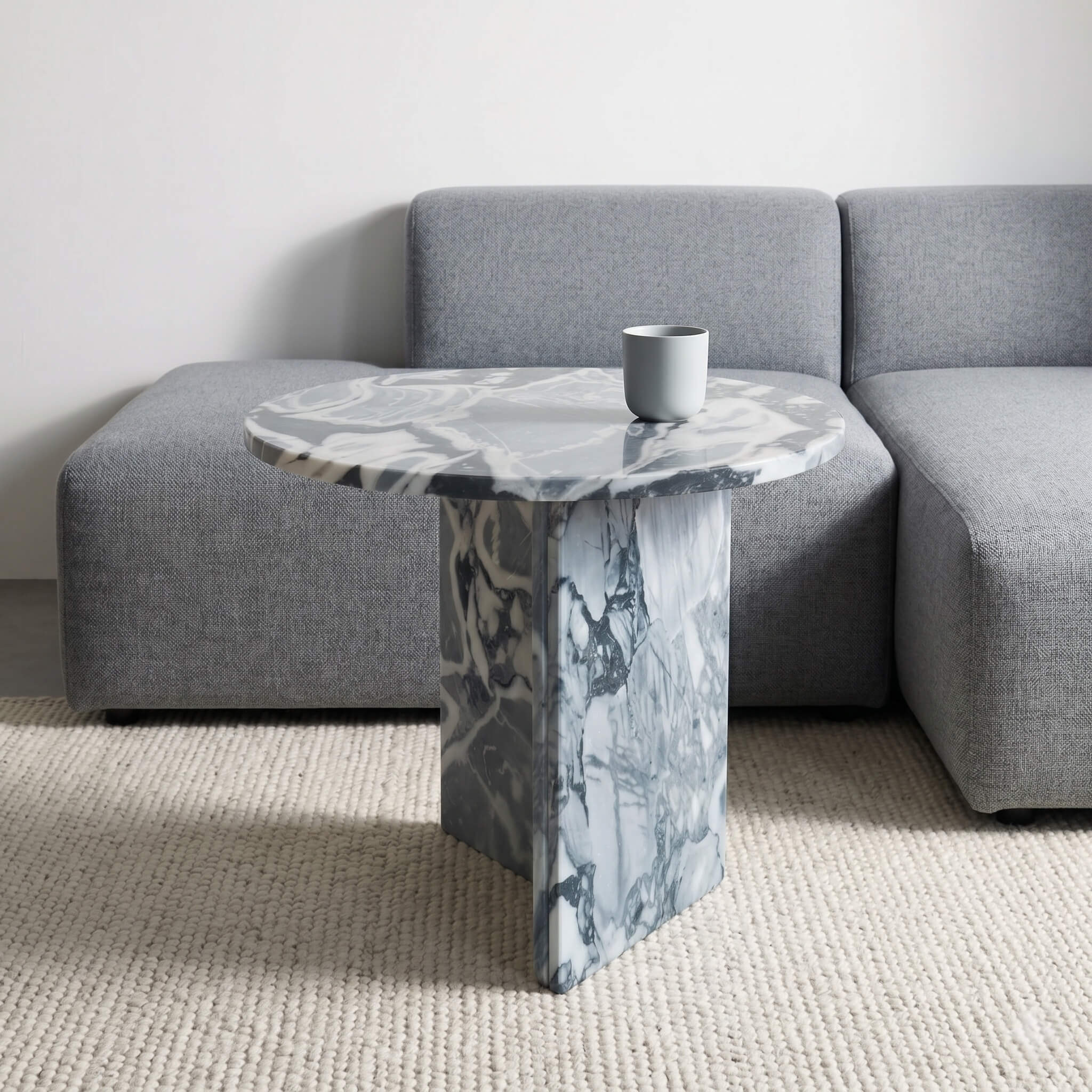 Cloudy blue marble side table styled beside gray modular sectional sofa, woven cream rug, minimalist living room with natural daylight.