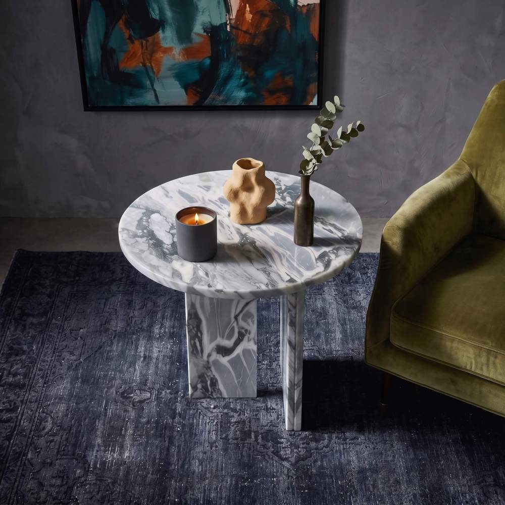 Cloudy blue marble side table in moody art lounge with olive velvet armchair, lit candle, sculptural ceramic vase, and abstract painting.