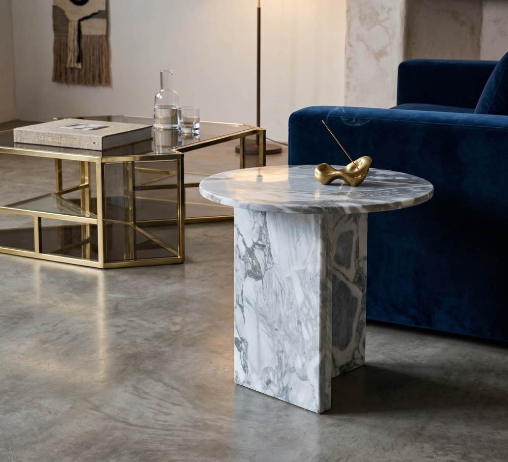Cloudy blue marble side table in modern loft with navy velvet sofa, brass-framed coffee table, polished concrete floor, and brass incense holder.