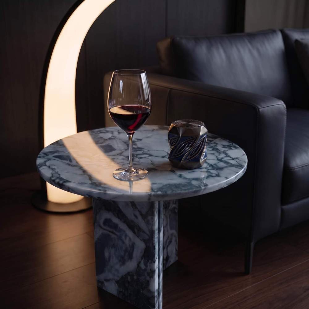 Cloudy blue marble side table in evening lounge setting with black leather sofa, arch floor lamp, red wine glass, and decor accent.