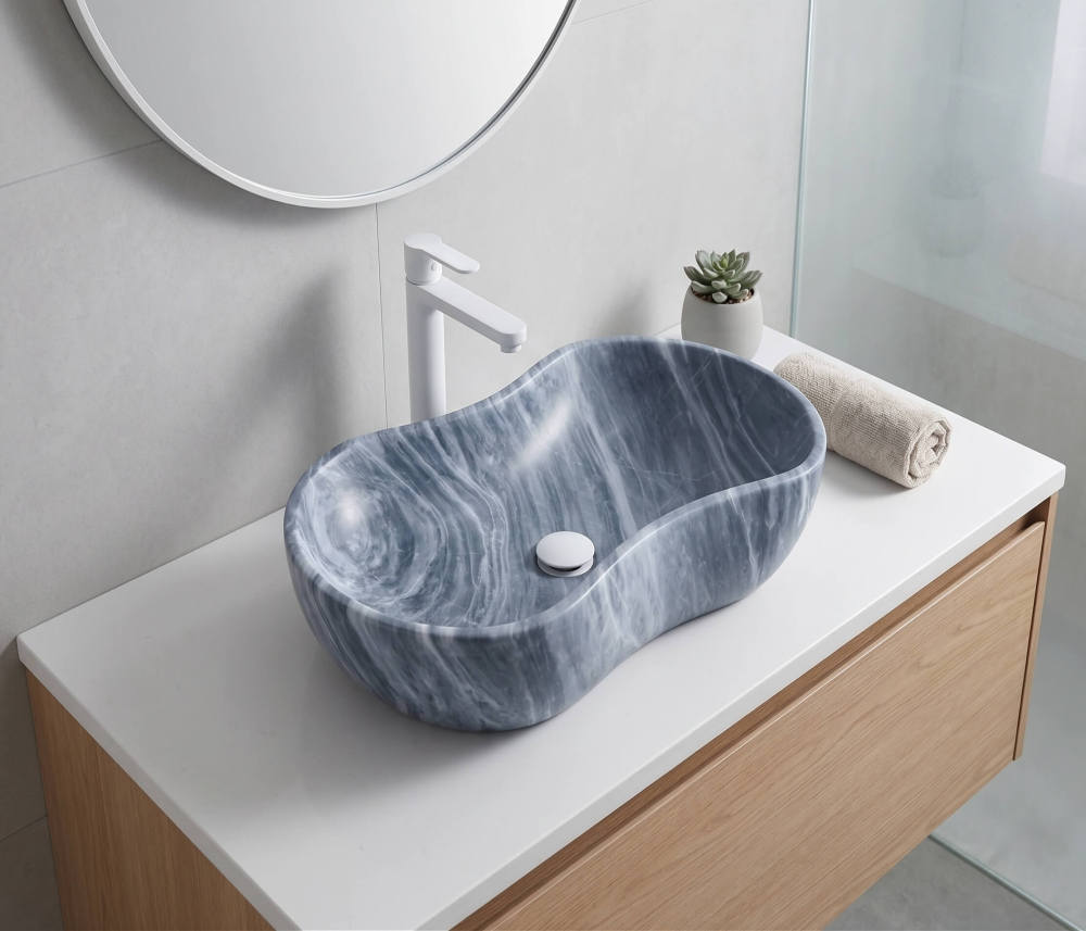 Carrara gray marble vessel sink on white quartz counter with matte white faucet and oak vanity in a light airy Nordic contemporary bathroom.