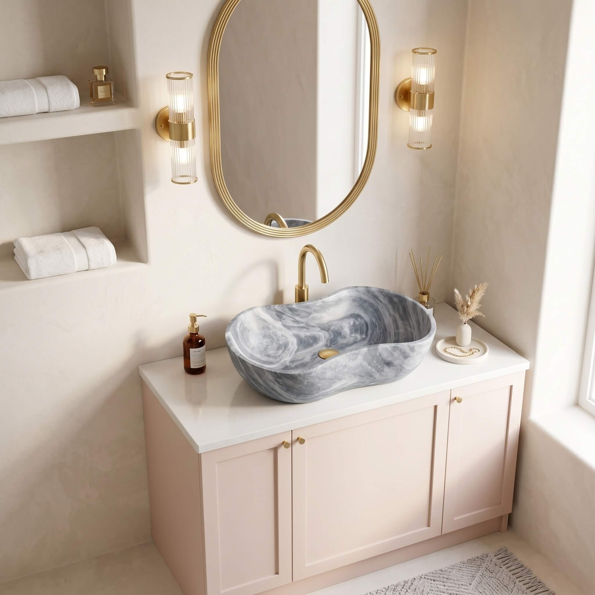 Carrara gray marble vessel sink with brushed brass faucet on blush vanity against limewashed plaster wall in a Mediterranean coastal bathroom.