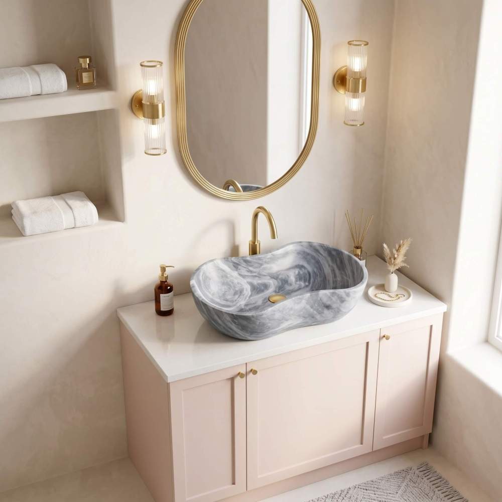Carrara gray marble vessel sink with brushed brass faucet on blush vanity against limewashed plaster wall in a Mediterranean coastal bathroom.