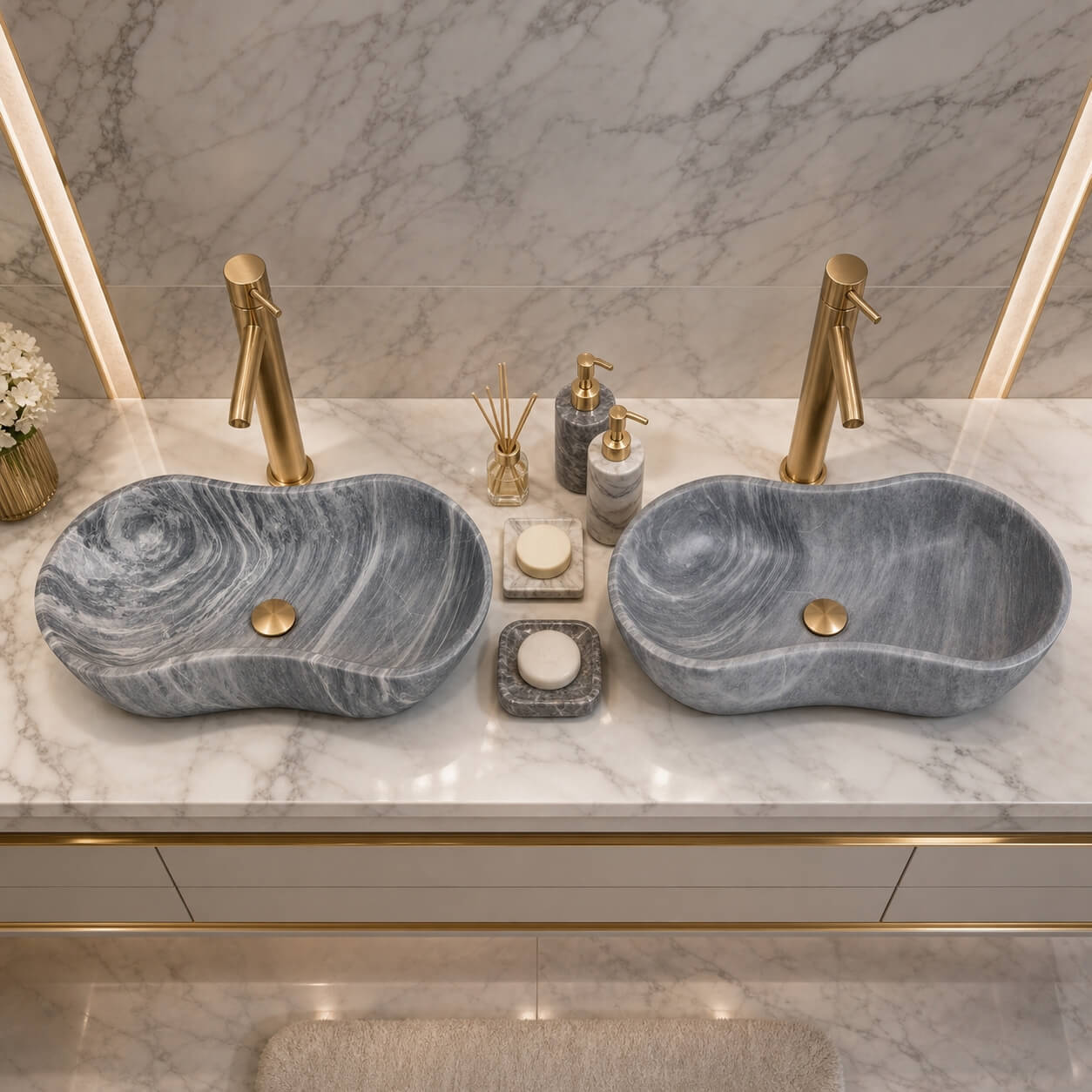 Top-down view of two Carrara gray marble vessel sinks paired with polished gold faucets on white Carrara countertop in a modern glam bathroom.