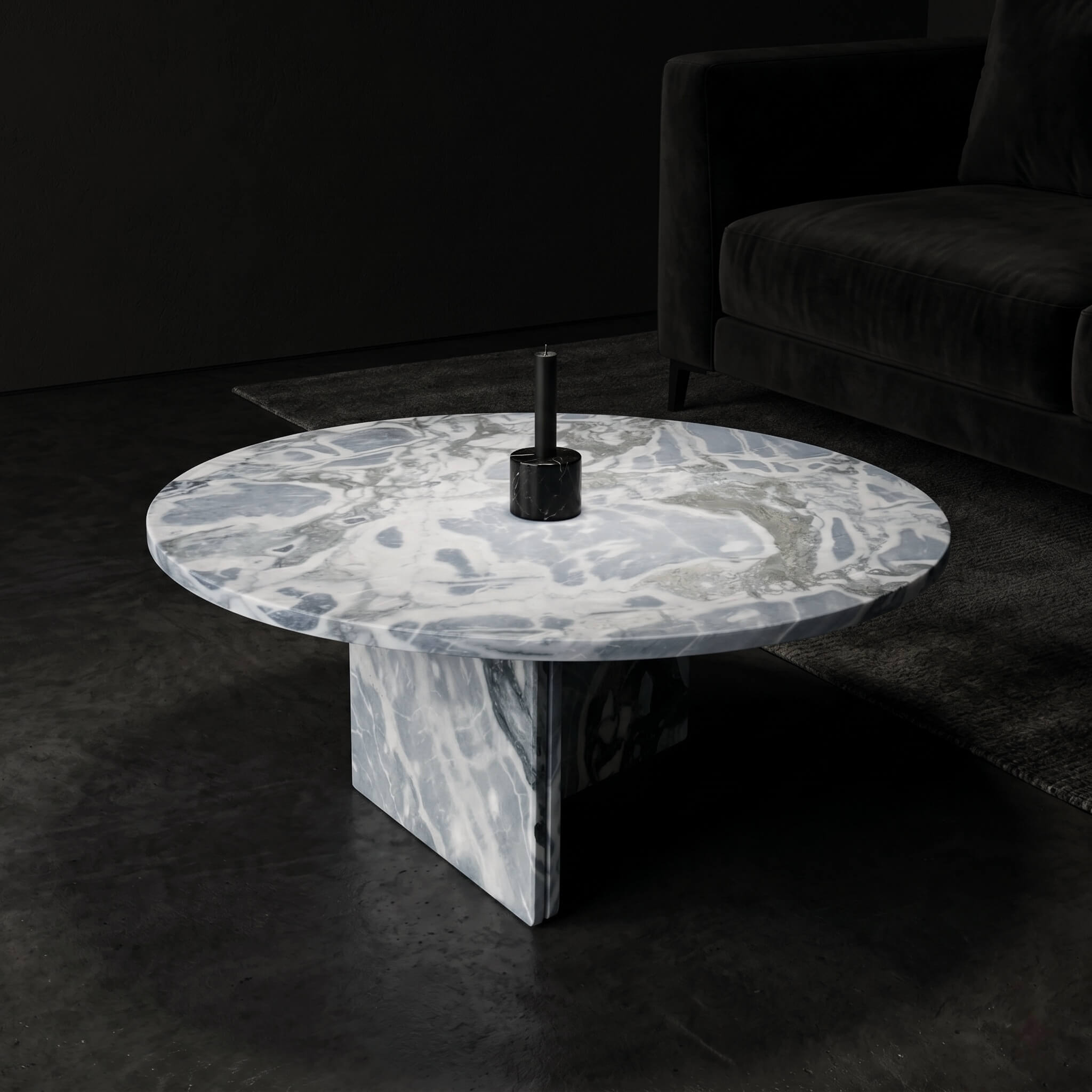 Cloudy blue marble coffee table in dark moody interior with black velvet sofa, black marble candle holder, and concrete-toned flooring.
