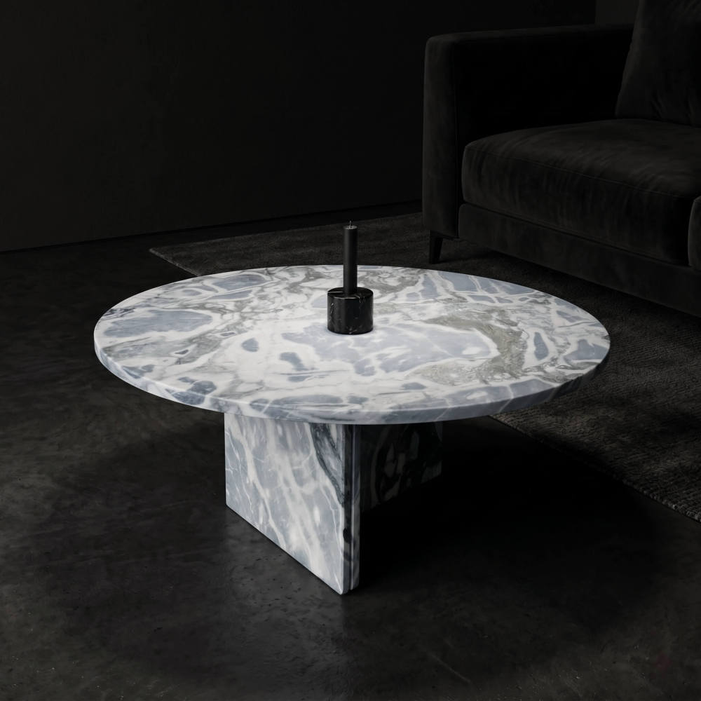 Cloudy blue marble coffee table in dark moody interior with black velvet sofa, black marble candle holder, and concrete-toned flooring.