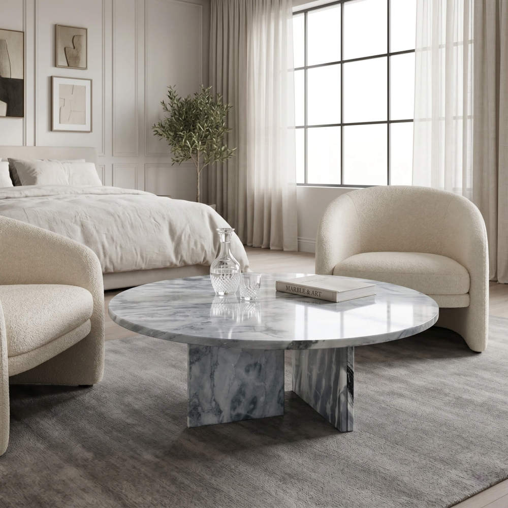 Cloudy blue marble coffee table in minimalist bedroom lounge with boucle armchairs, linen bedding, olive tree, and wainscoting.