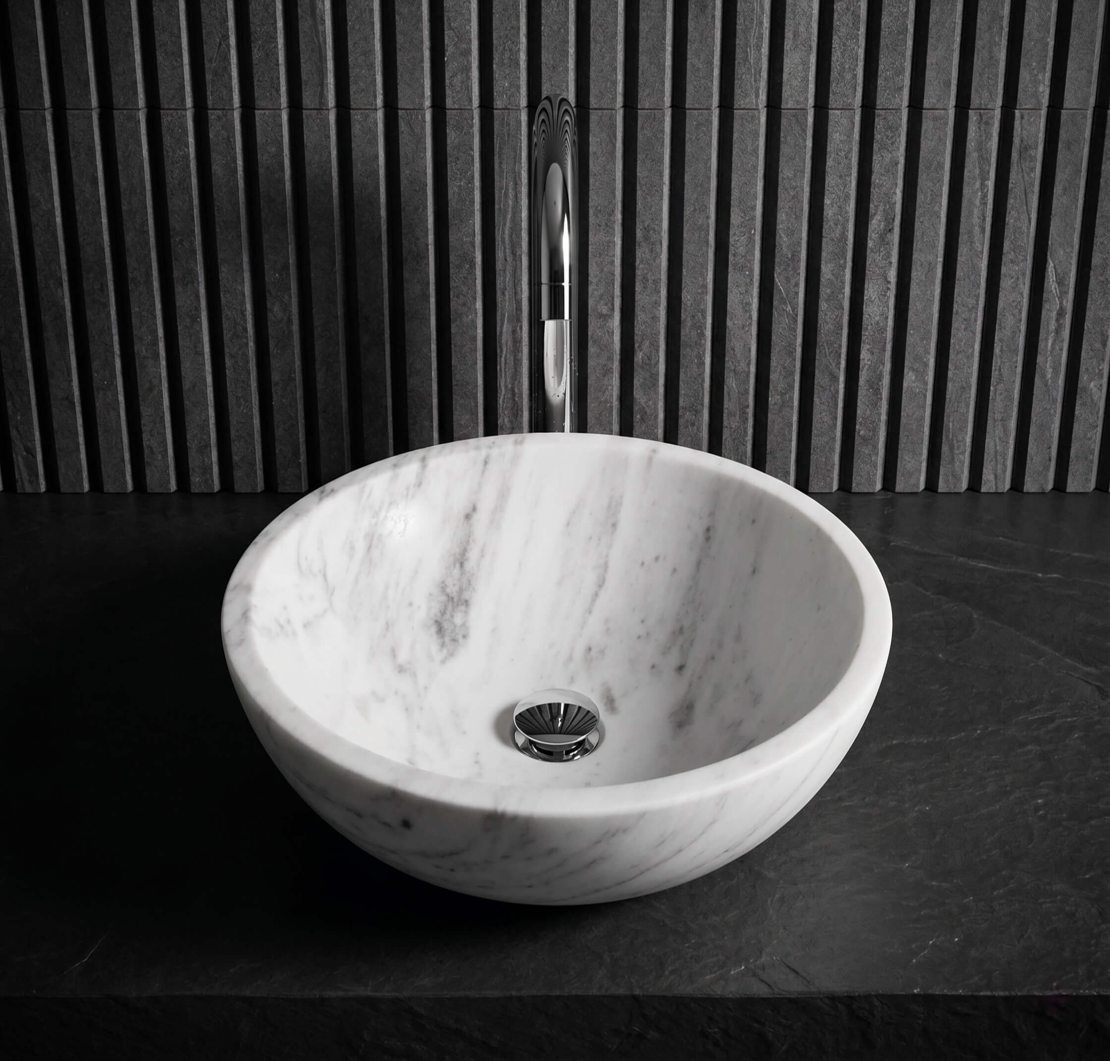 Front view of Snow Mountain white marble vessel sink on dark slate counter against fluted stone wall, modern minimalist bath.