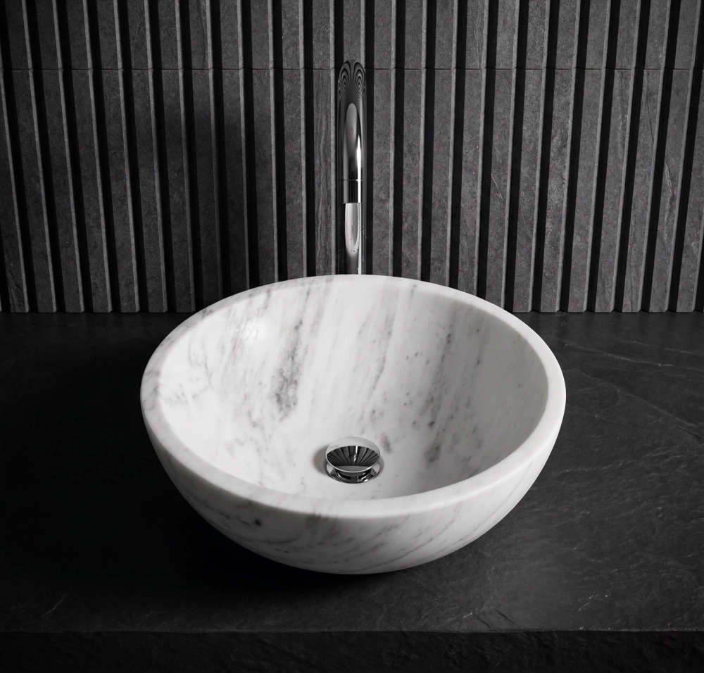 Front view of Snow Mountain white marble vessel sink on dark slate counter against fluted stone wall, modern minimalist bath.