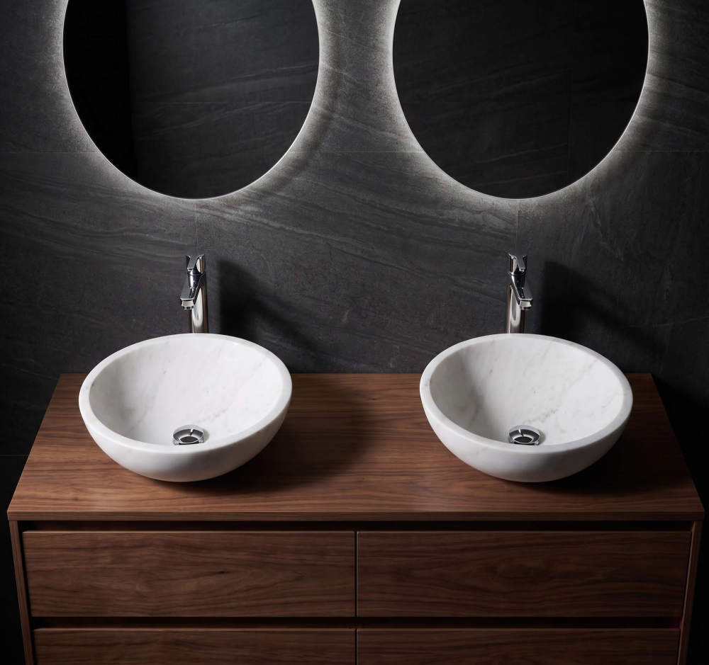 Snow Mountain white marble vessel sinks on walnut vanity, dark stone wall, backlit round mirrors, modern spa bathroom.