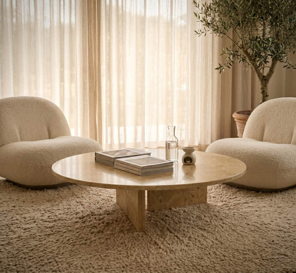 Round Hyatt Gold marble coffee table flanked by two cream bouclé lounge chairs in a sunlit quiet luxury sitting room.