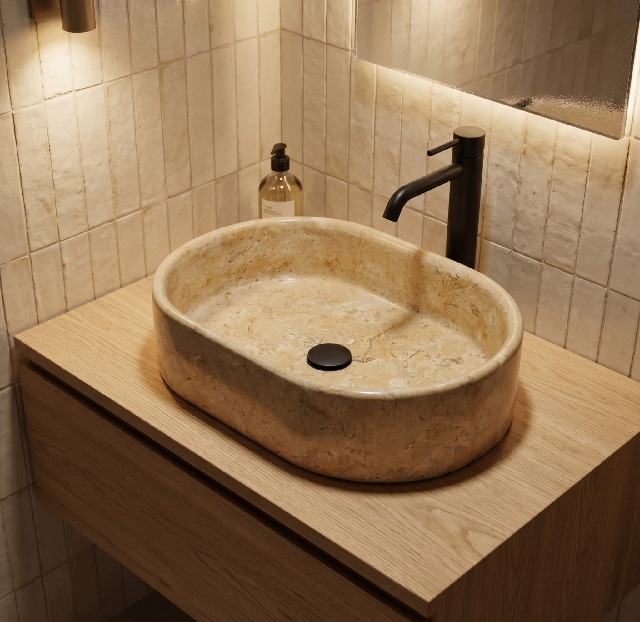 Amber Gold marble vessel sink on a wood floating vanity with matte black tall faucet against vertical cream zellige tile, warm cozy bathroom.