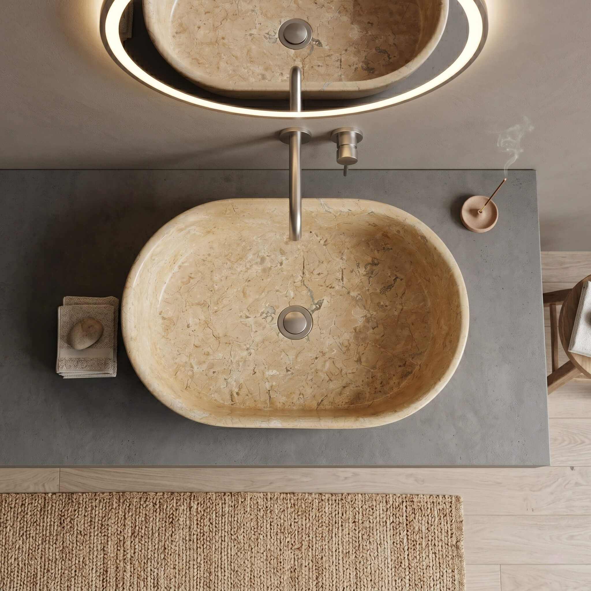 Aerial view of Amber Gold marble vessel sink on concrete vanity top with brushed silver wall-mount faucet, incense holder, and woven jute bath mat.