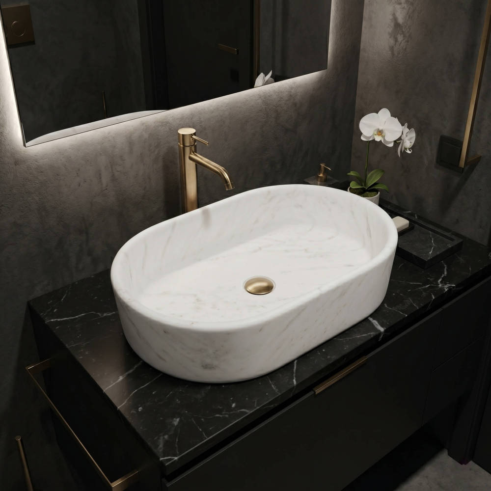 A Snow Mountain White marble oval vessel sink rests on a black marble top against microcement walls with a backlit mirror and gold faucet in a dark luxe bathroom.