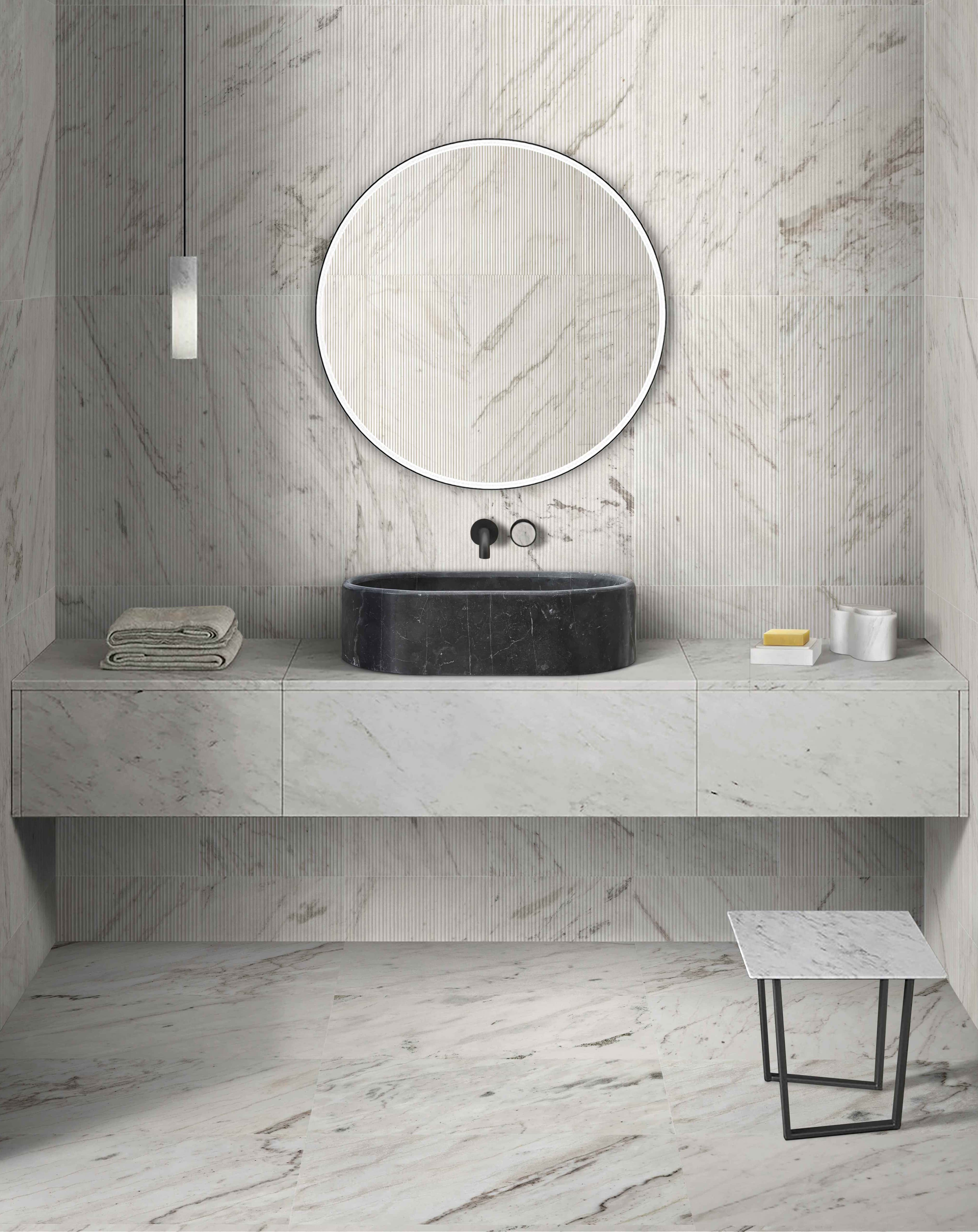 An Olive Black marble oval vessel sink with fluted Snow Mountain White textured wall tile and matching honed white stone accessories.